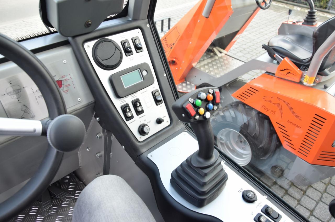 Wnętrze kabiny maszyny budowlanej z widocznym panelem sterowania, joystickiem z kolorowymi przyciskami oraz fragmentem pomarańczowej obudowy z napisem Pixy 25.
