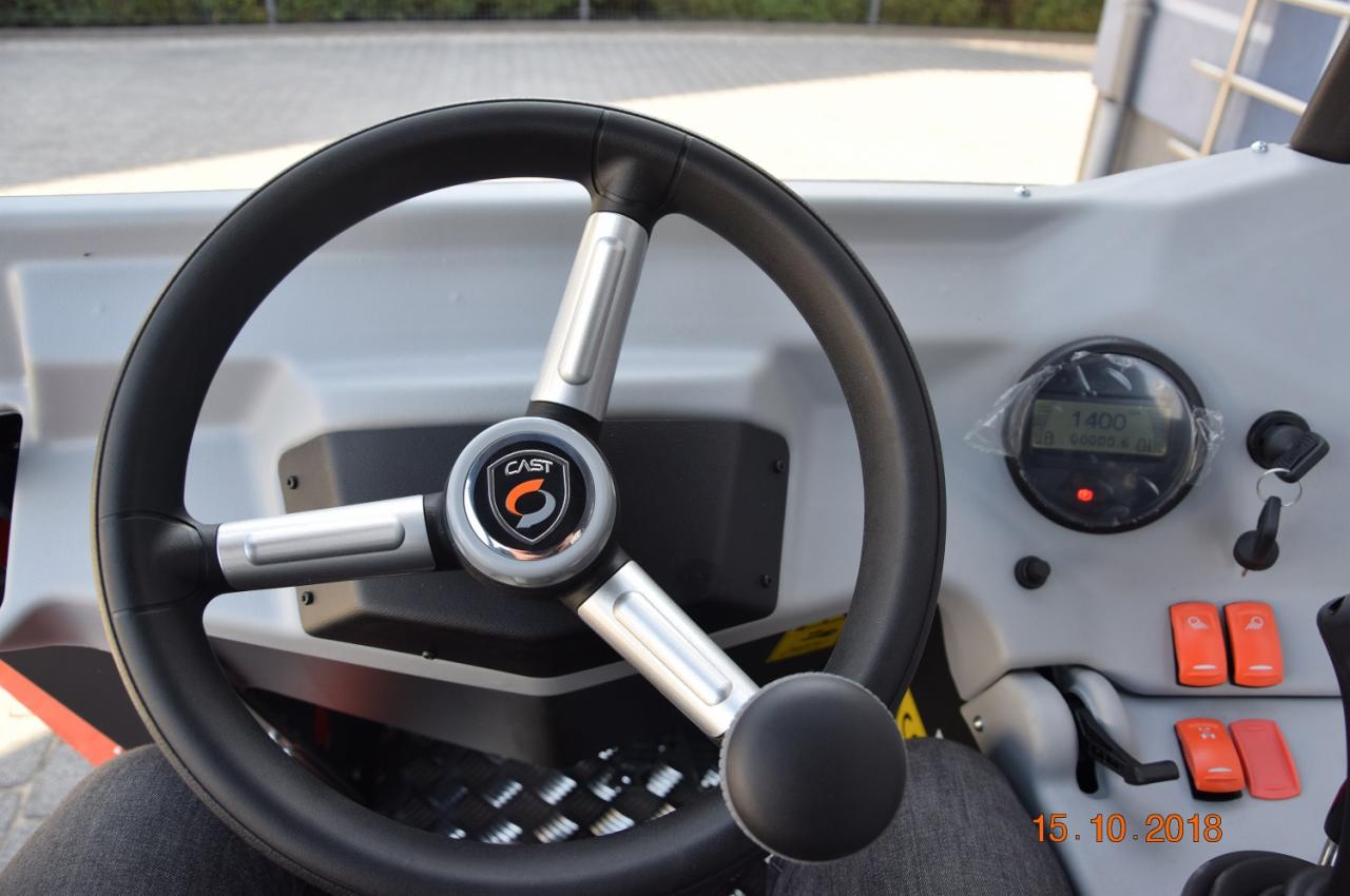 Wnętrze kabiny maszyny budowlanej z widoczną kierownicą z logo CAST, deską rozdzielczą z wyświetlaczem i przełącznikami.