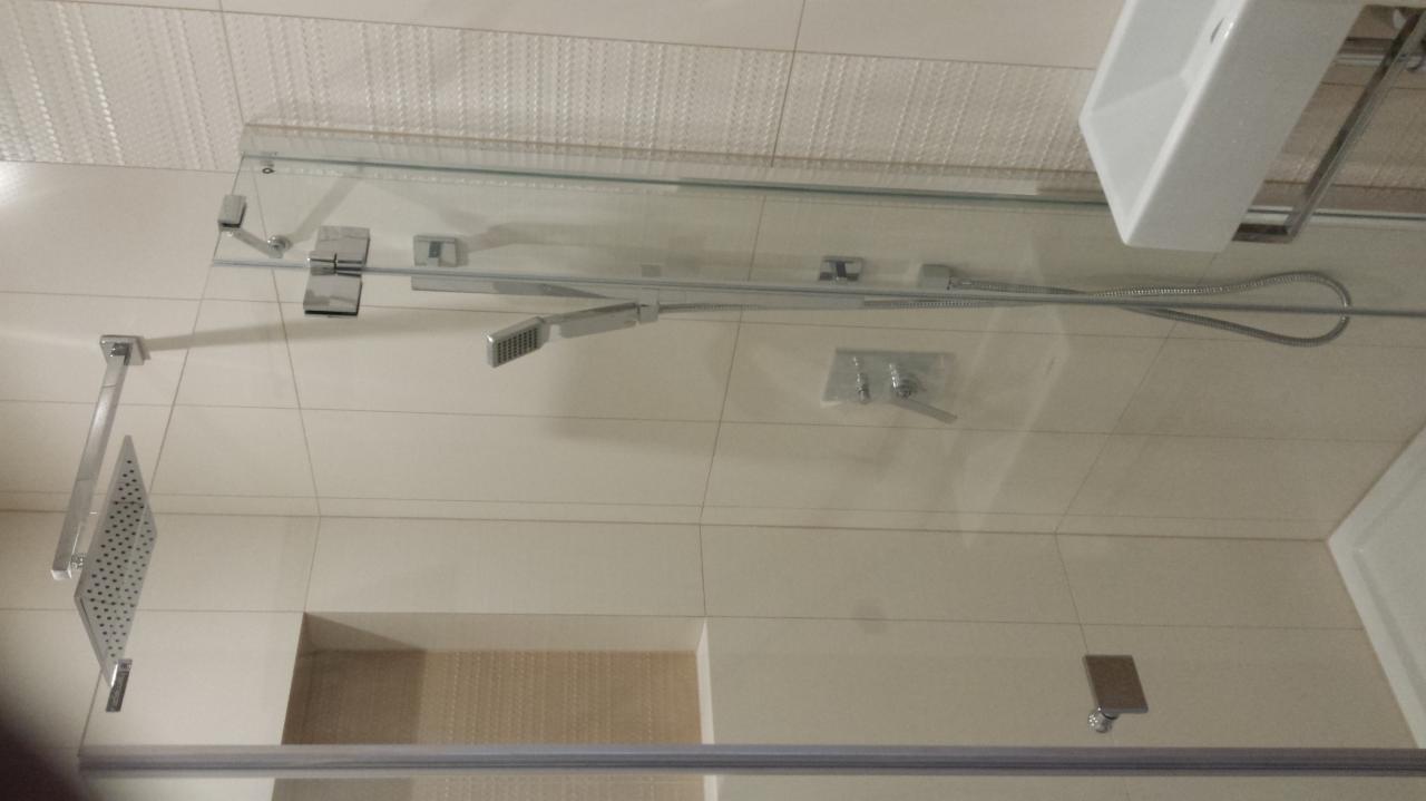 Nowoczesna kabina prysznicowa z deszczownicą i szklaną ścianką w wyremontowanej łazience, widok z dołu, beżowe płytki.