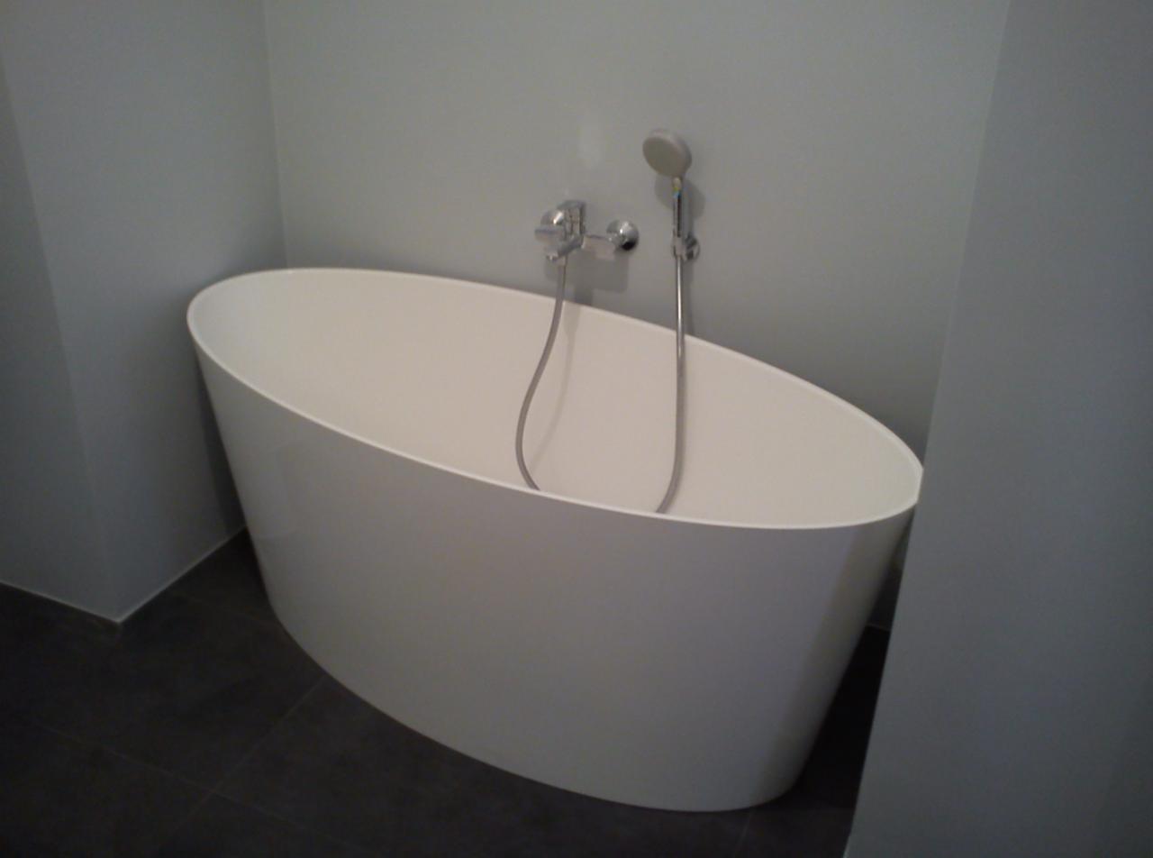 Nowoczesna, wolnostojąca wanna owalna z chromowaną armaturą i słuchawką prysznicową w minimalistycznej łazience z szarymi płytkami podłogowymi.