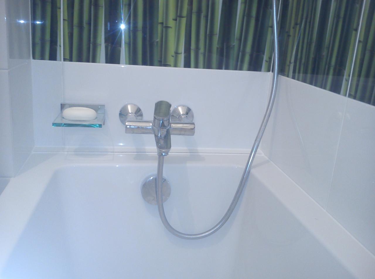 Biała wanna z chromowaną baterią i mydelniczką na tle ściany z motywem bambusa. Minimalistyczny design łazienki po remoncie, widok z góry na detale wykończenia.
