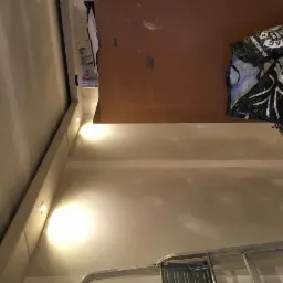 Ściana po szpachlowaniu, widoczne miejsca po łatach, przygotowana do malowania. W tle torba i fragment drabiny. Oświetlenie punktowe.