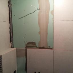 Przemysław Stawarski - Wnętrze łazienki w trakcie remontu, widoczne płyty kartonowo-gipsowe na ścianie, częściowo pokryte masą szpachlową, oraz ułożone płytki ceramiczne w różnych wzorach, w tym mozaika. Czerwona linia...