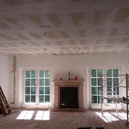 Przemysław Stawarski - Pokój w trakcie remontu: sufit z widocznymi płytami kartonowo-gipsowymi przed szpachlowaniem, ściany częściowo zagruntowane, widoczne kable elektryczne, drabina drewniana i rusztowanie aluminiowe...