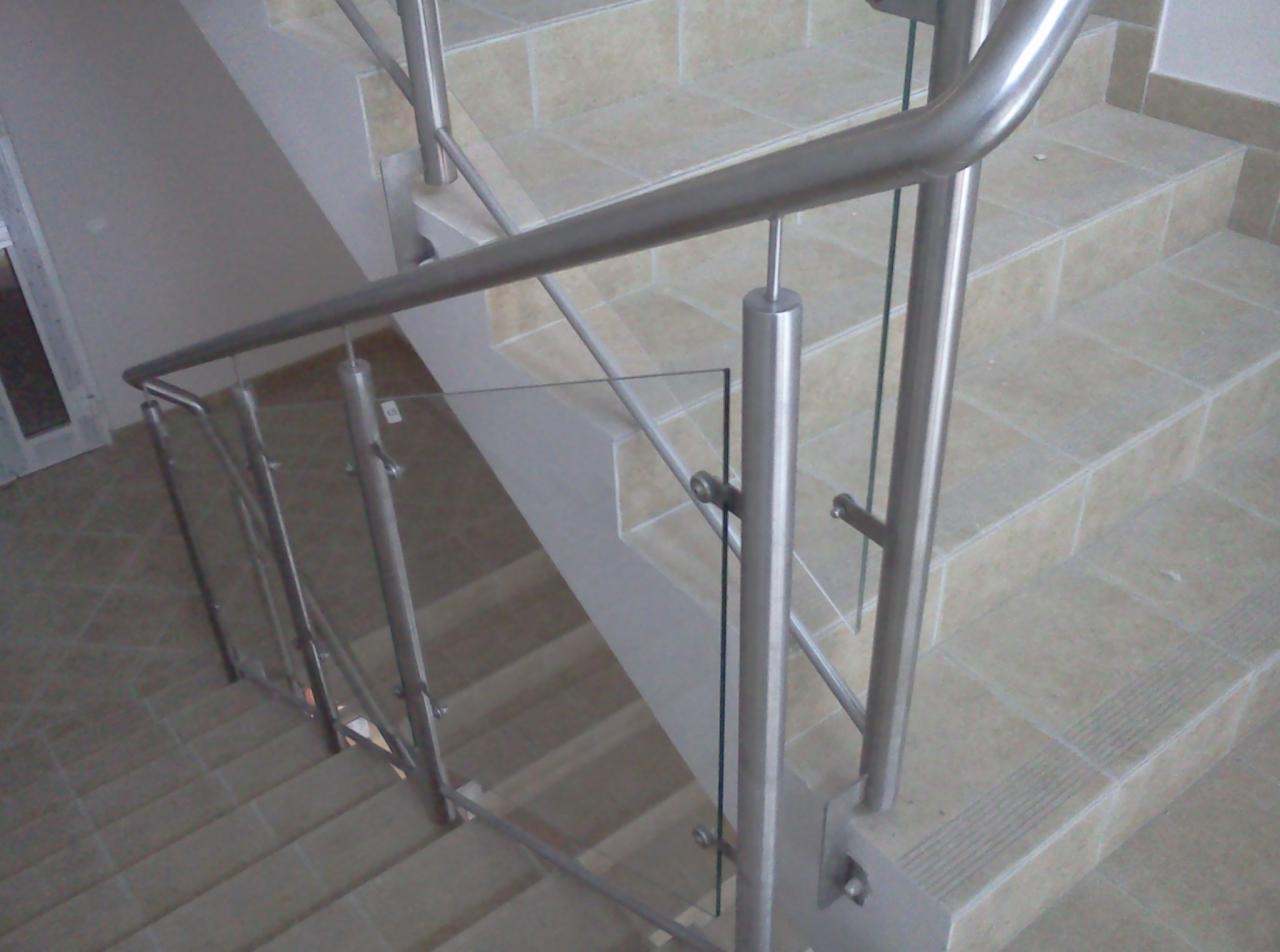 Schody z beżowymi płytkami i nowoczesną balustradą ze stali nierdzewnej i szkła, mocowaną do stopni za pomocą śrub.