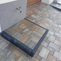 SM2 Mateusz Salamon - Ułożona kostka brukowa z ciemną obwódką na schodach wejściowych do domu, widoczny kran na elewacji.