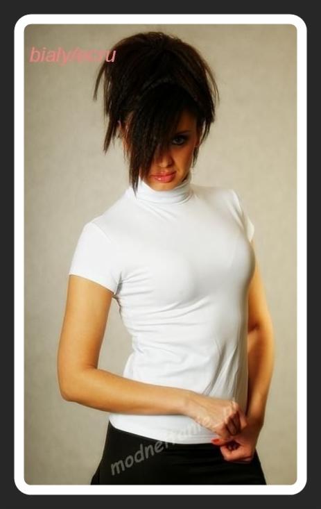 Portret kobiety w białym golfie z krótkim rękawem i czarnej spódnicy na neutralnym tle. Włosy upięte do góry, część opada na twarz. Ujęcie od pasa w górę.