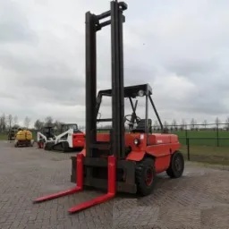 Czerwony wózek widłowy spalinowy marki Lansing na brukowanym placu, z innymi maszynami budowlanymi w tle pod pochmurnym niebem.