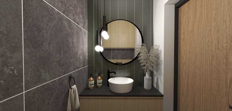 Nowoczesna łazienka z ciemnoszarą, płytkową ścianą, okrągłym lustrem z podświetleniem, białą umywalką nablatową, czarną armaturą i drewnianą szafką pod umywalką; na blacie dwie butelki...