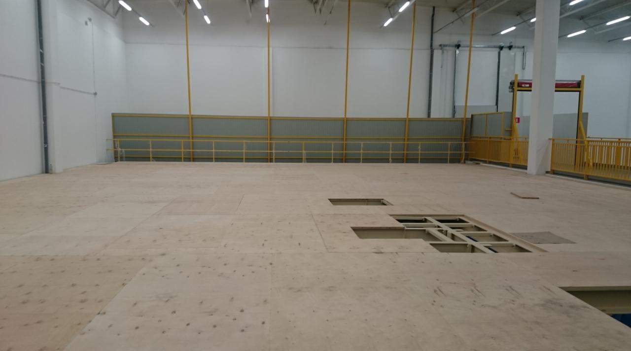 Montaż podłogi z płyt drewnopochodnych w hali magazynowej, widoczne otwory rewizyjne w podłodze i żółte barierki zabezpieczające.