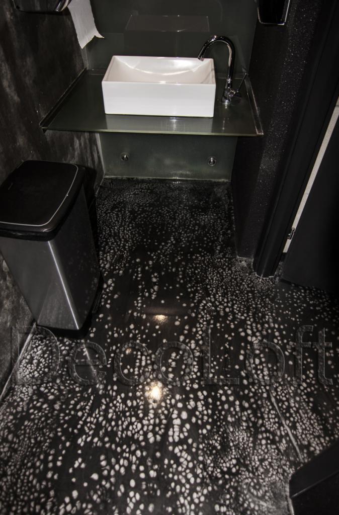 Czarno-biała posadzka w łazience z umywalką i koszem na śmieci. Posadzka z unikalnym wzorem przypominającym plamy.
