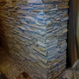 Wykończenie narożnika ściany dekoracyjnym kamieniem w odcieniach beżu i szarości, widoczne drobne odpryski na podłodze.