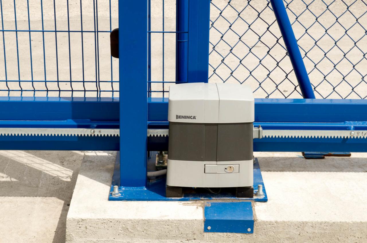 Szczegółowe ujęcie napędu marki Beninca zamontowanego na niebieskiej, przesuwnej bramie z siatki, umieszczonego na betonowej podstawie.