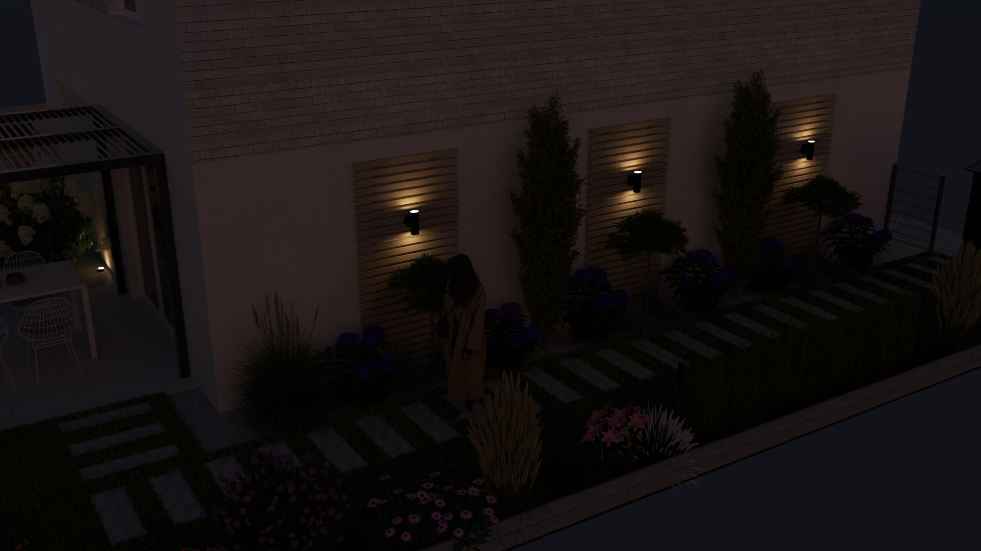 Oświetlony ogród w Działdowie nocą: ścieżka z płyt, rabaty kwiatowe, drzewa i pergola z oświetleniem. Dekoracyjne panele z lampami na ścianie budynku.