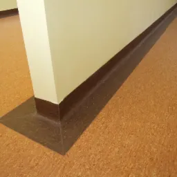 Korek na podłodze z ciemnobrązową listwą przypodłogową i wykończeniem słupa. Podłoga o jednolitej, drobnej strukturze i ciepłej kolorystyce.