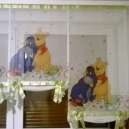 Dwu-częściowa roleta rzymska z motywem Kubusia Puchatka i Kłapouchego, upięta zielonymi wstążkami, zamontowana na oknie z żaluzjami.