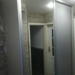 Zamontowane przesuwne drzwi szafy wnękowej z widocznym wnętrzem łazienki z czarnymi płytkami i dekoracyjną ścianą w tle.