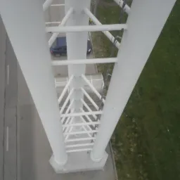 Wysoka, biała konstrukcja stalowa widziana z góry, z fragmentem parkingu, samochodu i trawnika w tle. Układ w kształcie litery V.