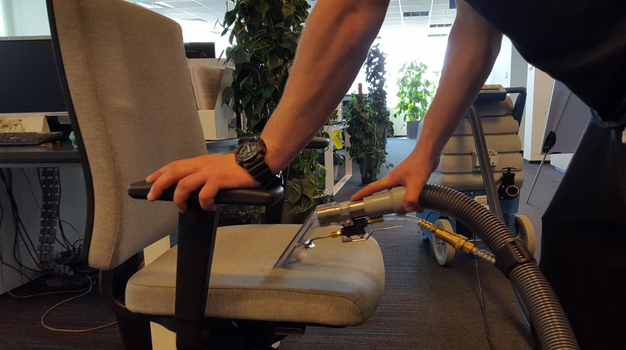 Czyszczenie tapicerki krzesła biurowego za pomocą profesjonalnego odkurzacza piorącego. Widoczne rośliny biurowe w tle.