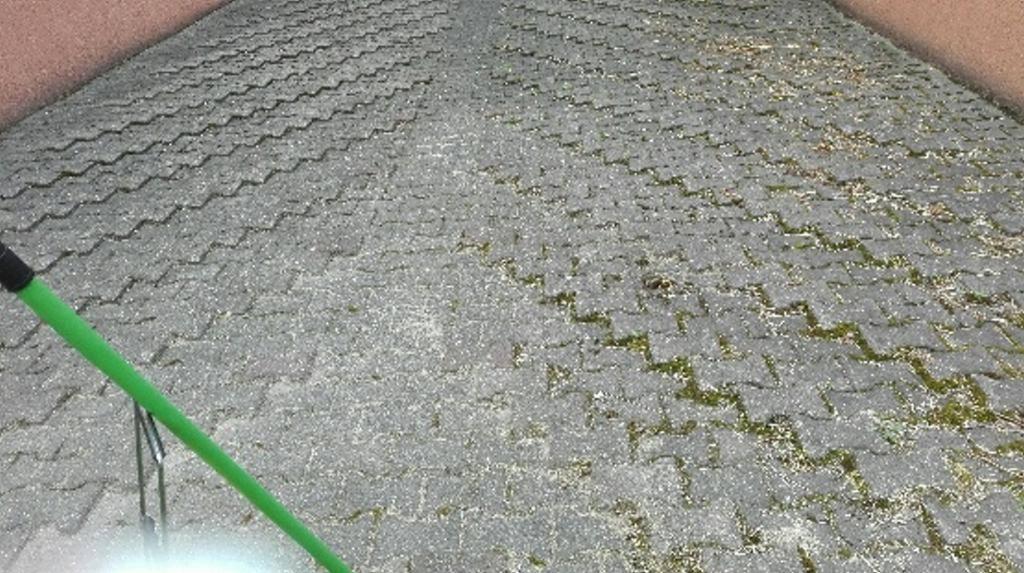 Czyszczenie kostki brukowej z zielonymi wykwitami i resztkami organicznymi za pomocą myjki ciśnieniowej z długą lancą.