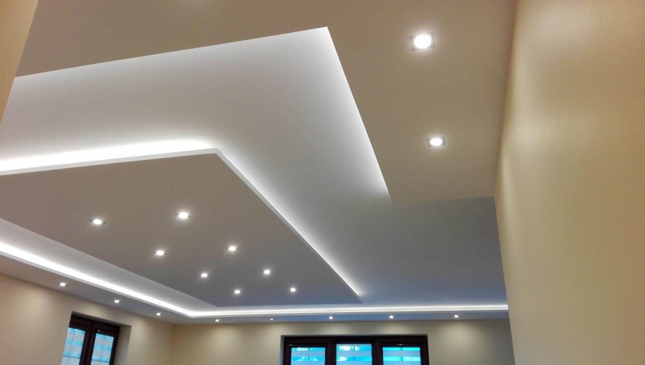 Nowoczesny sufit podwieszany z oświetleniem LED, widoczne okna i ściany w neutralnych barwach.