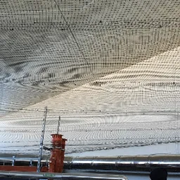 Siatka zabezpieczająca rozpięta pod sufitem, widoczne rury wentylacyjne i elementy instalacji przemysłowej.