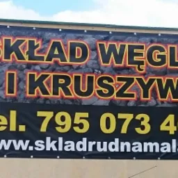 Reklama składu węgla i kruszyw z numerem telefonu i adresem strony internetowej na banerze reklamowym przy budynku.