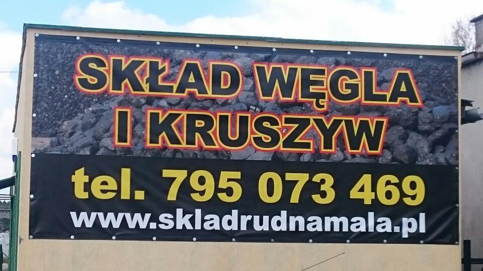 Reklama składu węgla i kruszyw z numerem telefonu i adresem strony internetowej na banerze reklamowym przy budynku.