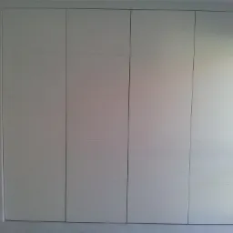 Biała szafa wnękowa z czterema drzwiami, minimalistyczny design, widoczna ceglana ściana w tle przez otwarte drzwi po lewej stronie.