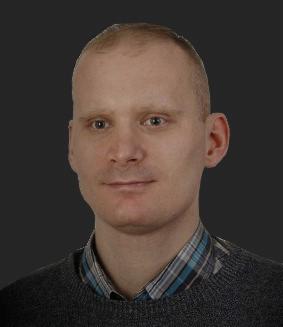 Portret mężczyzny w szarym swetrze i koszuli w kratę na ciemnoszarym tle.