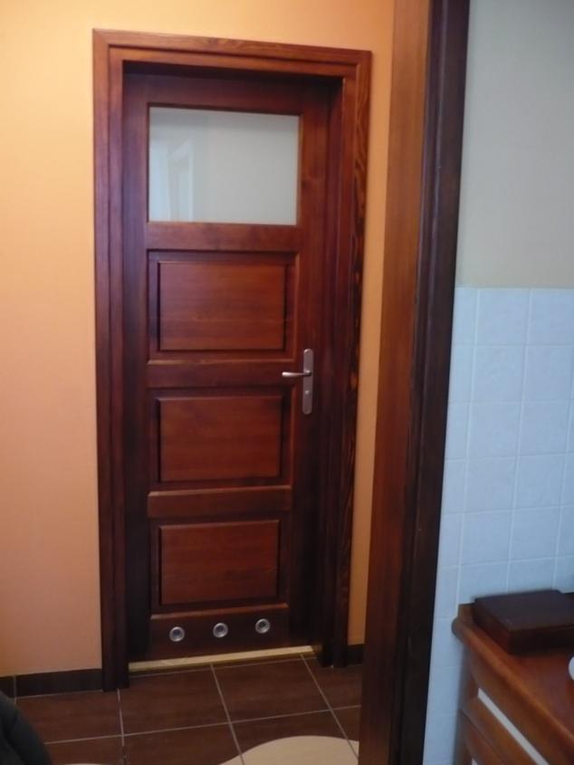 Ciemnobrązowe drzwi wewnętrzne z szybą i trzema panelami, zamontowane w ościeżnicy, widoczne trzy okrągłe otwory wentylacyjne u dołu.