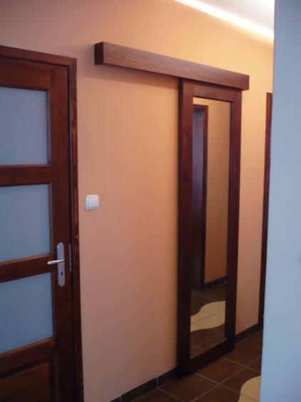 Wnętrze z przesuwnymi drzwiami w drewnianej ramie i klasycznymi drzwiami z przeszkleniami, obie w odcieniach brązu, na tle ściany w kolorze ciepłego beżu.