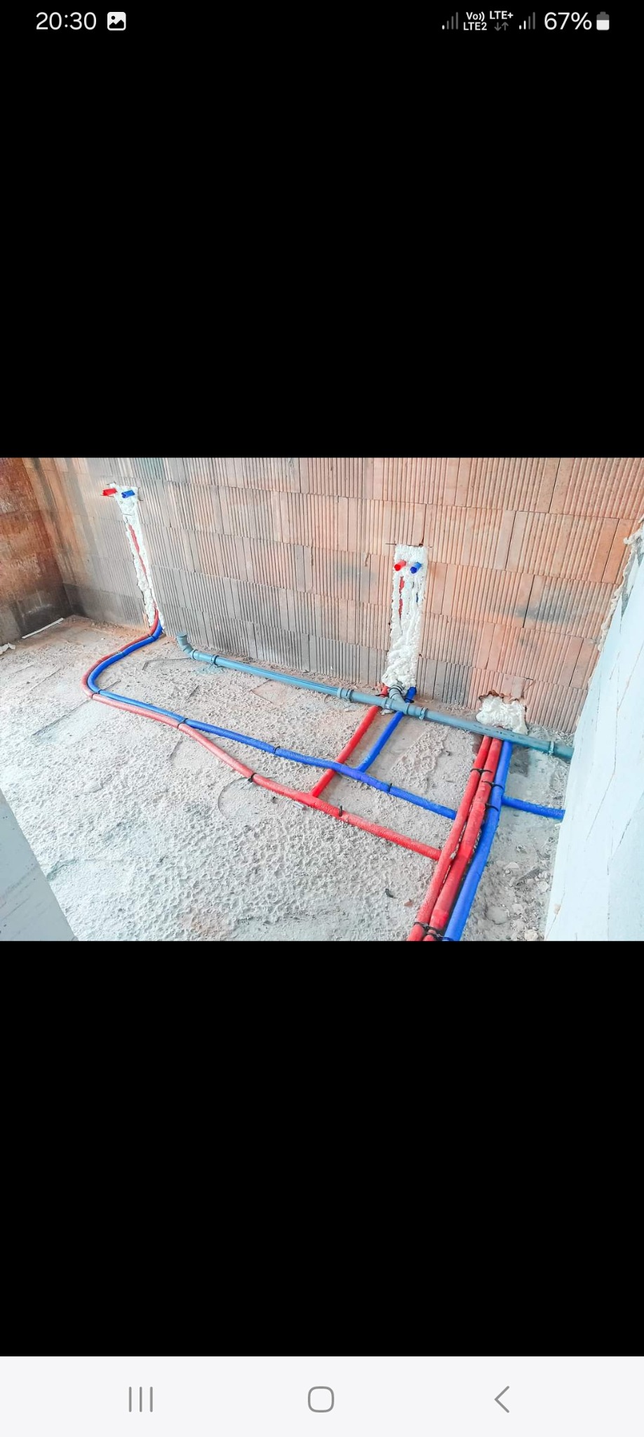 Wykonywanie instalacji wodno-kanalizacyjnej: czerwono-niebieskie rury prowadzone po podłodze w surowym pomieszczeniu z ceglanymi ścianami, pianką montażową uszczelnione podejścia do instalacji.