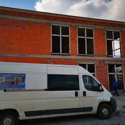 P.H.U. KWADRO Sebastian Lorenz - Montaż okien w surowym budynku z czerwonej cegły, biały samochód dostawczy z reklamą firmy na pierwszym planie.