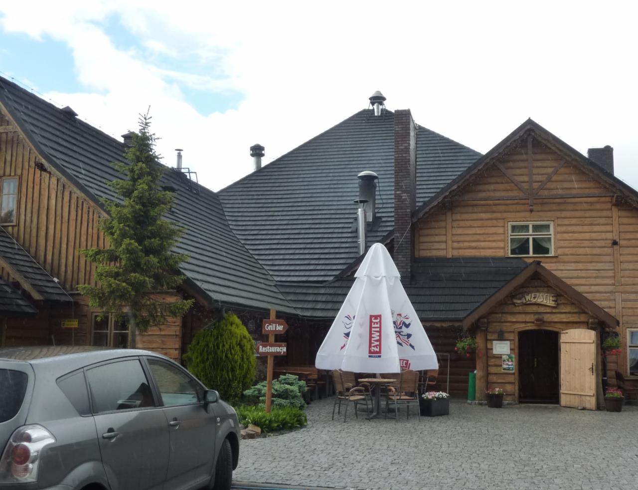 Drewniany budynek grill baru w stylu regionalnym z ciemnym dachem i parasolem reklamowym, Walichnowy.