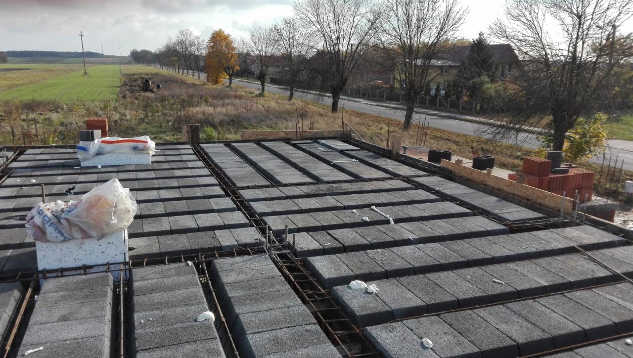 Wieniec stropowy z szalunkiem i zbrojeniem na budowie domu jednorodzinnego, widok z góry na szare bloczki i stalowe pręty, w tle wieś Osjaków.