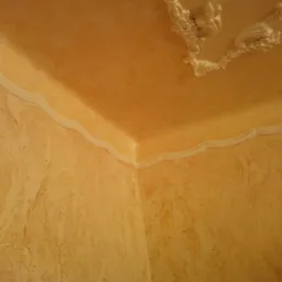 Dekoracyjne wykończenie wnętrza: ściany i sufit w odcieniach beżu z ozdobnymi listwami i rozetą, faktura imitująca marmur, ciepłe oświetlenie.