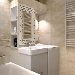 Beżowa łazienka z umywalką, lustrem w geometrycznej ramie i grzejnikiem drabinkowym. Widoczna wanna i półki z kosmetykami. Ciepłe oświetlenie.