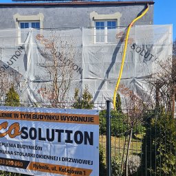 Eco Solution Rybnik - Budynek w trakcie ocieplania elewacji, osłonięty siatką z nadrukowanym logo firmy EcoSolution, na pierwszym planie baner reklamowy tej samej firmy.