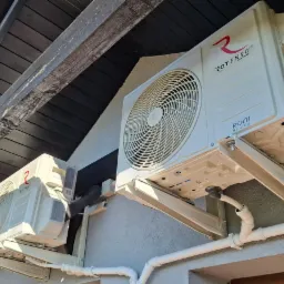 Dwie jednostki zewnętrzne klimatyzacji Rotenso Roni Series zamontowane na elewacji domu z widocznymi elementami instalacji i drewnianą podbitką dachu.