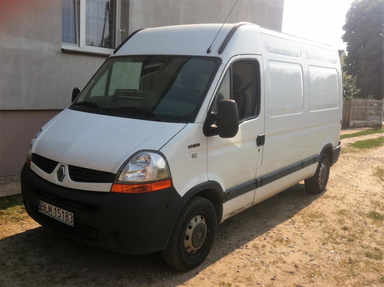 Biały, wysoki furgon Renault Master z anteną na dachu, zaparkowany przed budynkiem mieszkalnym. Widoczna tablica rejestracyjna.