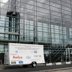Przyczepa reklamowa z logo sponsorów (Amica, HSBC) przed budynkiem ze szklaną fasadą. Billboard na kółkach, ekspozycja zewnętrzna.