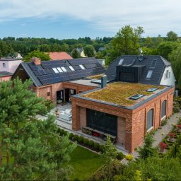 Budrop - Widok z góry na nowoczesny dom z cegły z panelami słonecznymi na dachu i zielonym dachem, otoczony bujną zielenią.