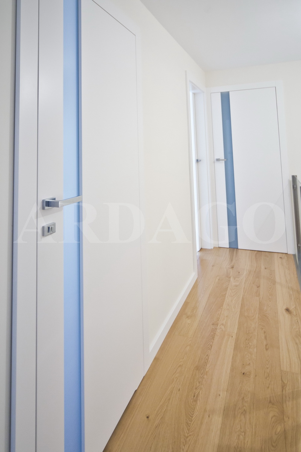 Nowoczesne, białe drzwi wewnętrzne z niebieskim akcentem, widoczne na jasnym korytarzu z drewnianą podłogą.