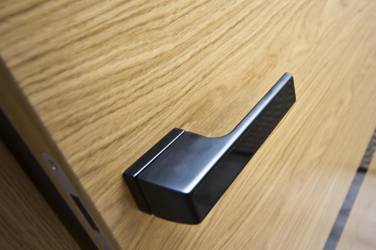 Czarny, matowy uchwyt na jasnym, dębowym skrzydle z widocznym usłojeniem.