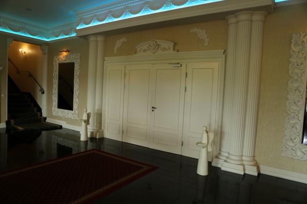 Eleganckie, kremowe drzwi wewnętrzne z dekoracyjnymi kolumnami i sztukaterią, oświetlone niebieskim światłem, na połyskującej podłodze z dywanem.