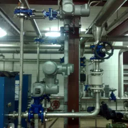 Instalacja przemysłowa z rurami, zaworami i elementami sterującymi, widoczny niebieski panel urządzenia z napisem 'SONIC TECHNOLOGY' oraz fragment drabiny w tle.