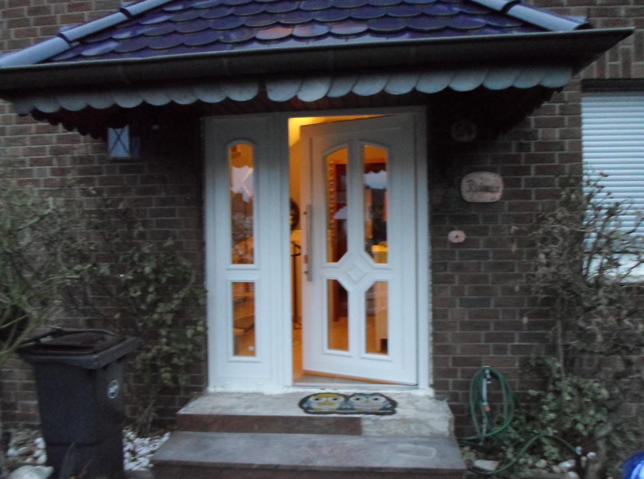 Otwarta, biała, przeszklona stolarka drzwiowa wejściowa, z dekoracyjnym wzorem, zamontowana w domu z cegły. Widoczny podest wejściowy i wycieraczka z motywem sowy.