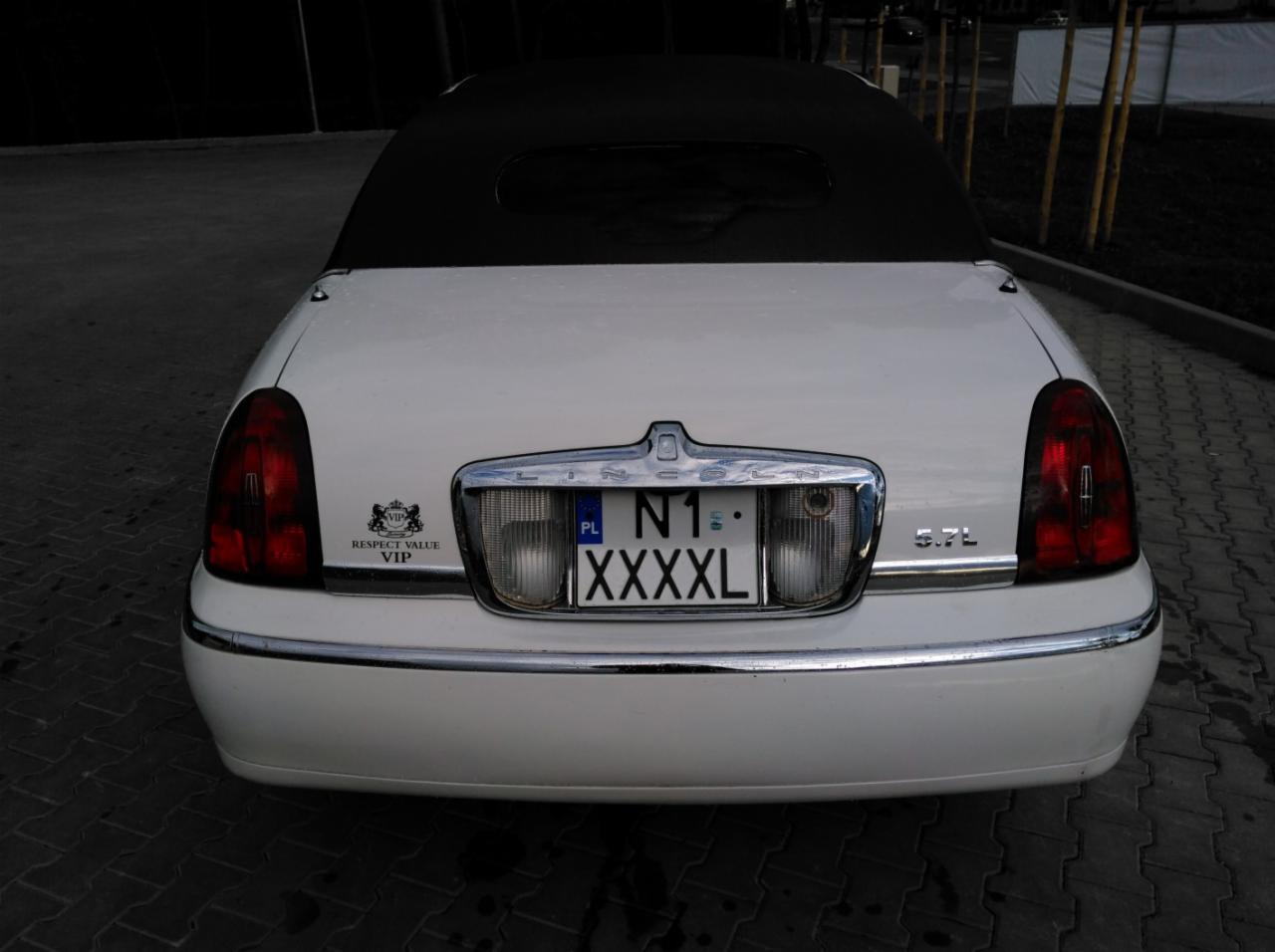 Tył białej limuzyny Lincoln w Olsztynie z czarnym dachem typu kabriolet, widoczne tablice rejestracyjne, emblemat VIP i oznaczenie silnika 5.7L.