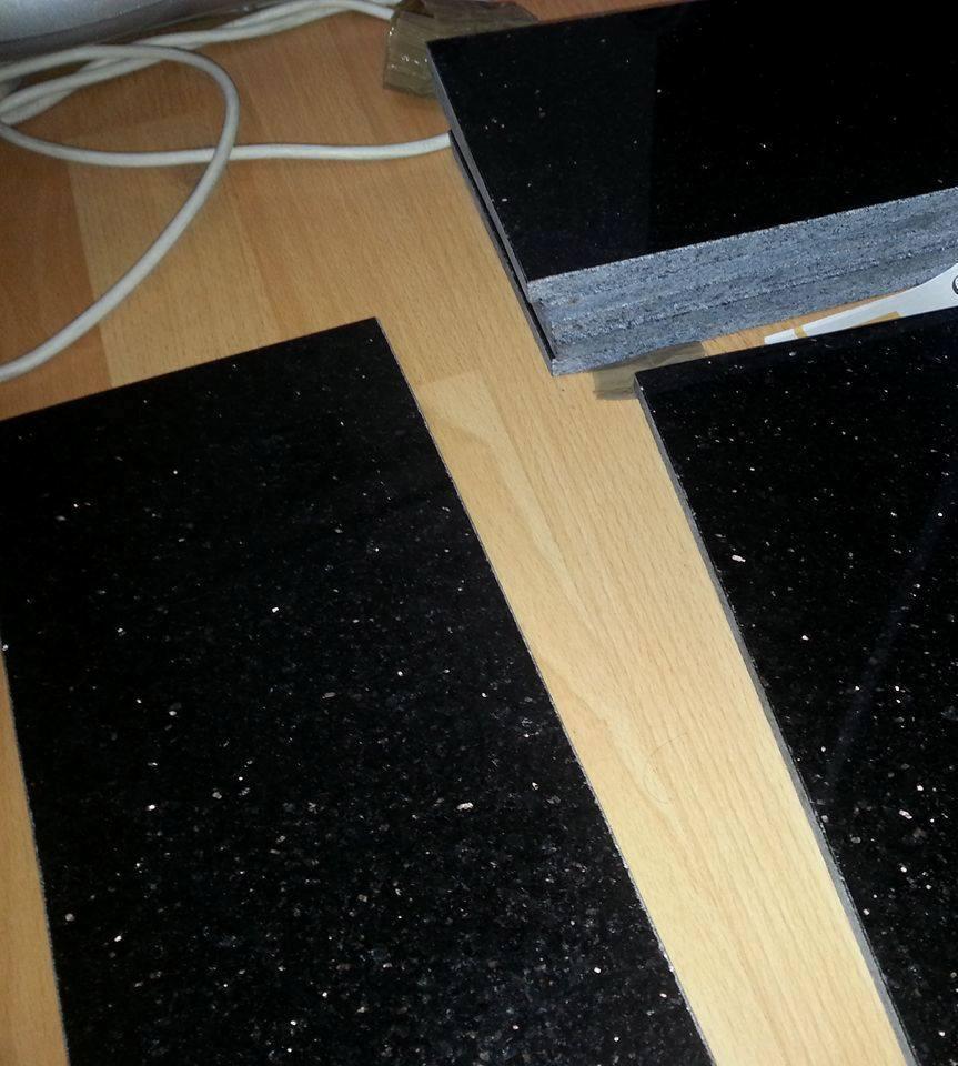 Czarne, błyszczące płytki z efektem gwiazd, ułożone na drewnianej podłodze. Widoczny stos płytek oraz fragment kabla w górnej części kadru.